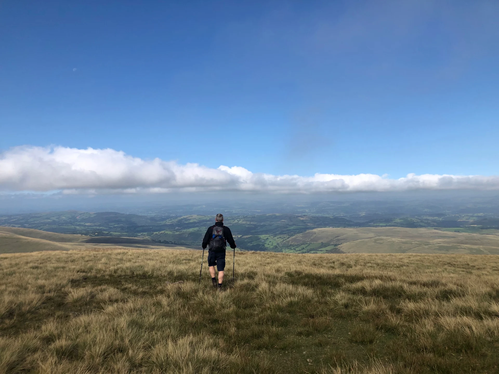 Hiker on grassy hill with cloudy sky