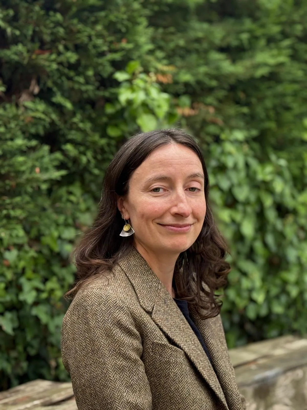 Smiling woman in tweed blazer before green foliage