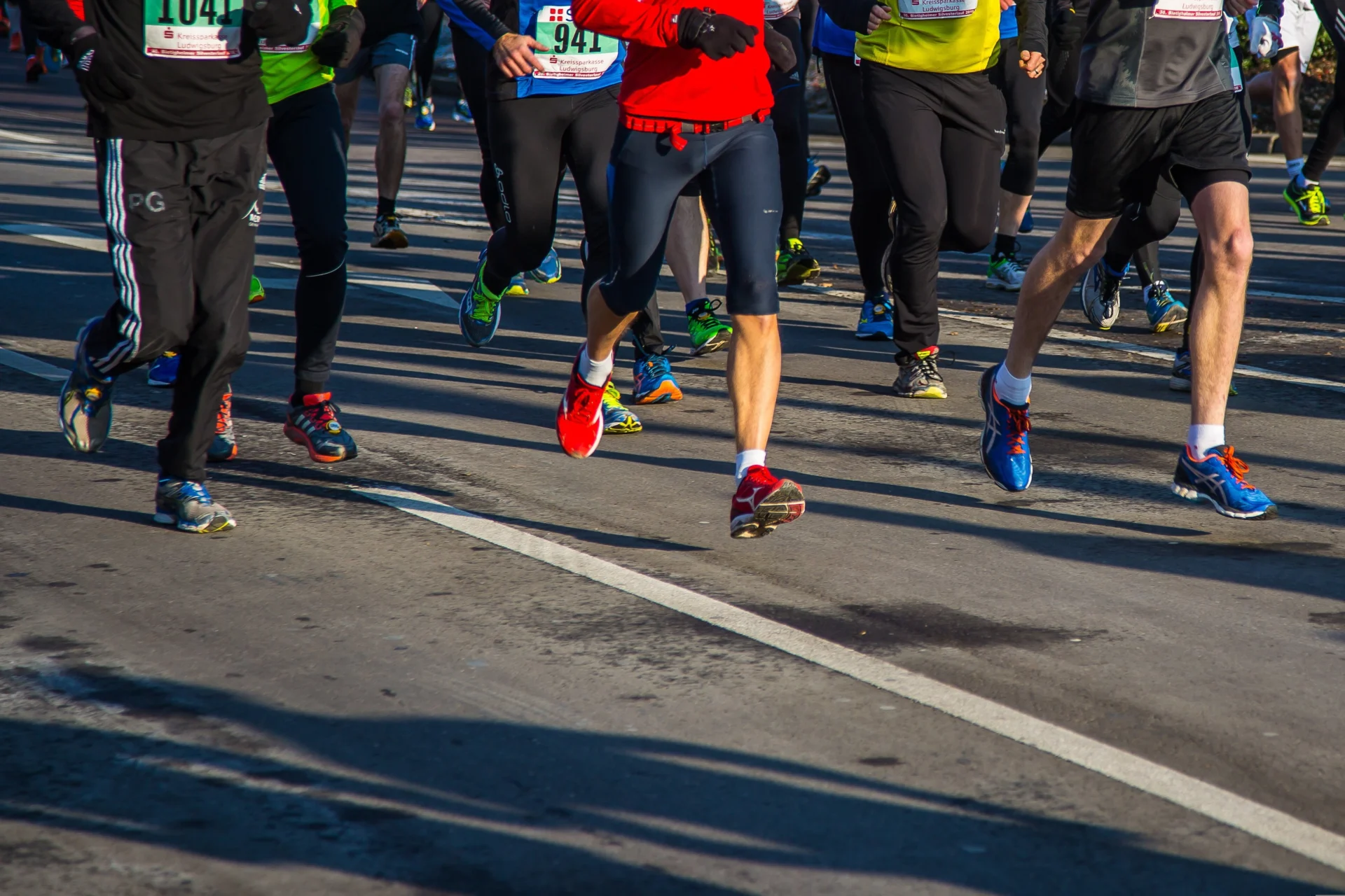 Runners wearing colorful shoes race along a sunlit road